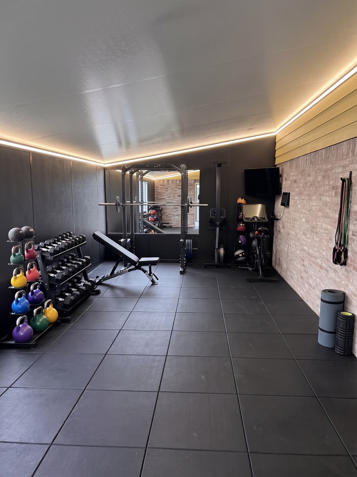 Finished private home gym interior with dumbbells, kettlebells, power rack and warm cove lighting